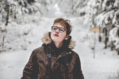 白天，一名身穿黑色连帽夹克的男子站在积雪覆盖的大树旁